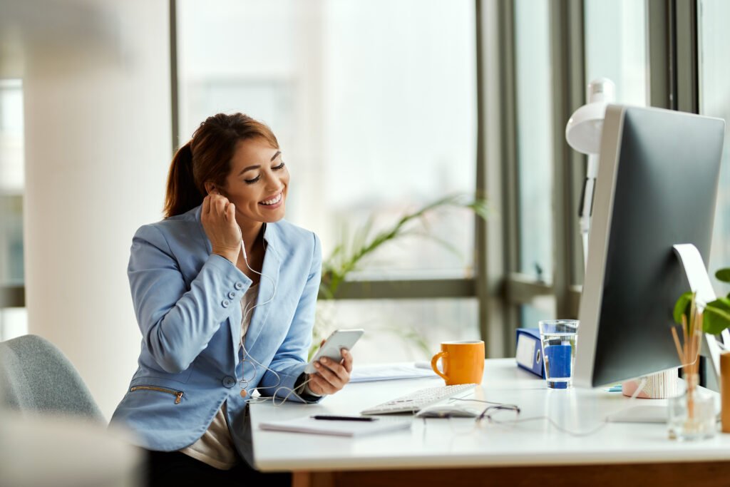 smiling businesswoman adjusting earphones while using smart phon